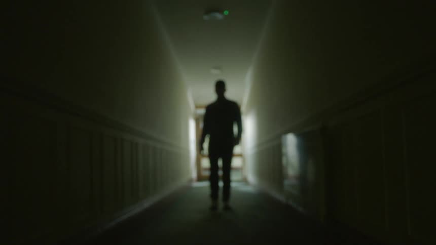A man is walking through a dark corridor in a building