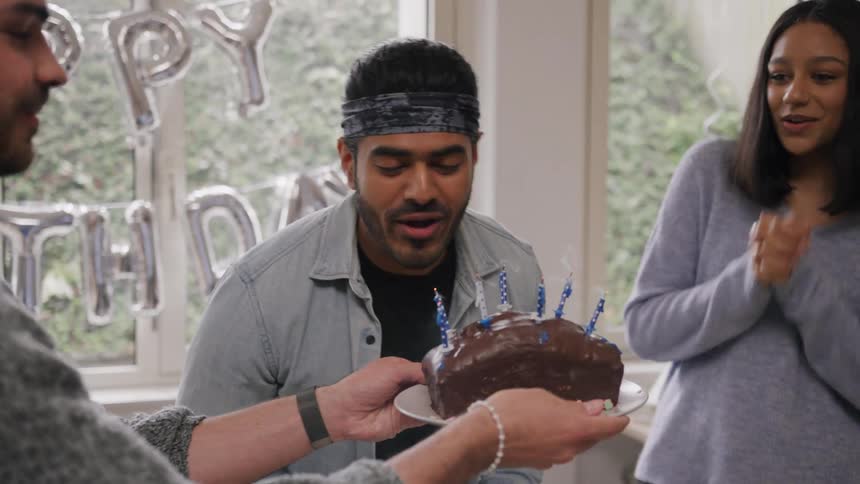 Man blowing out birthday candles and celebrating with coworkers at the office