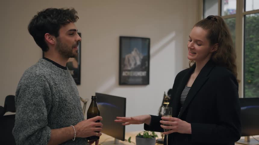 Man and woman talking while holding a bottle and a glass of wine inside an office in the morning