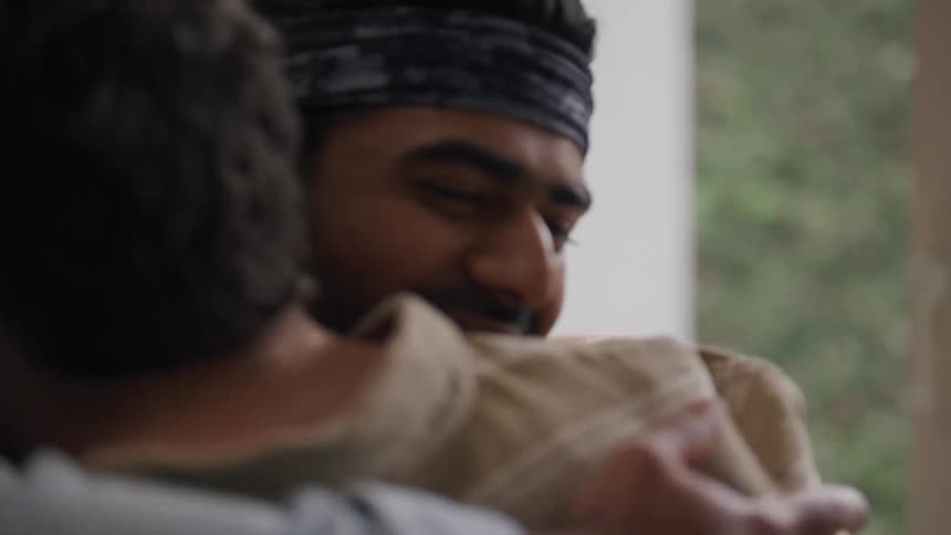 Two men warmly embrace in a heartfelt hug smiling with visible emotion