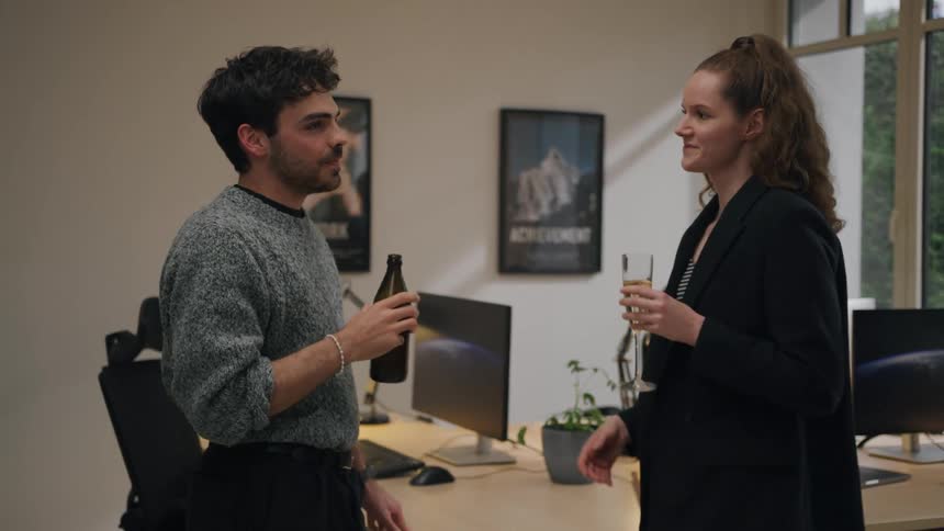 A man and woman smile while drinking and chatting in a modern office
