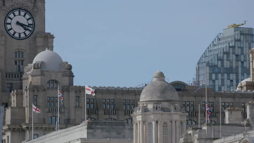 Flags wave in the breeze outside a building with a tower and clock