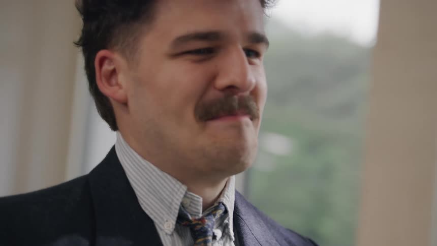 A man wearing a suit and sporting a mustache looks happy as he highfives another man