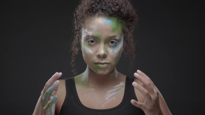 A woman's face and hands are covered with colorful face paint