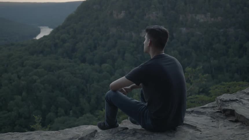 A man sits on the edge of a cliff looking at a view