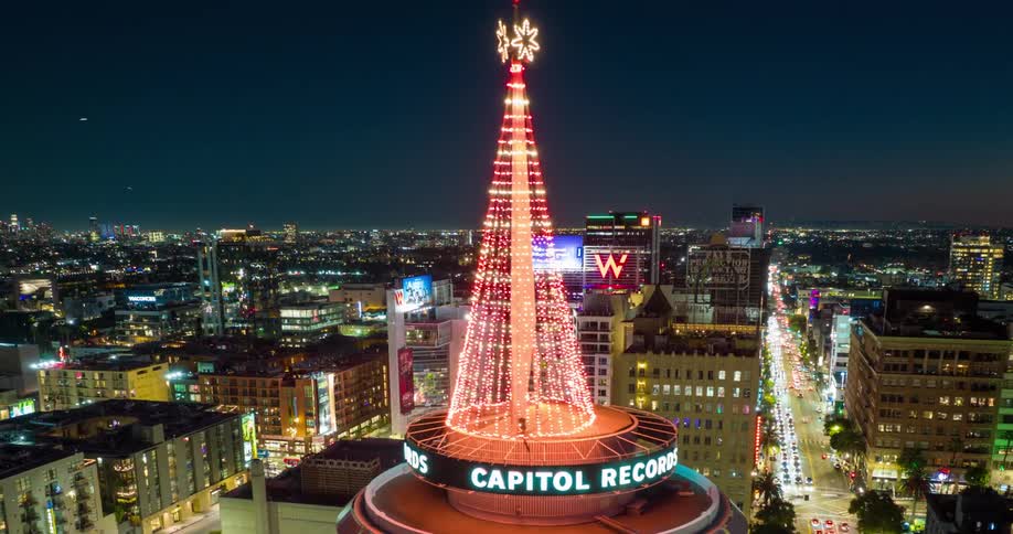 Drone orbits Capitol Records building in Los Angeles lit with red holiday lights in nighttime cityscape
