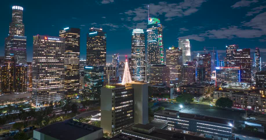 Traffic passes through a brightly lit Los Angeles at night also passing a roof top decoration composed of strings of lights