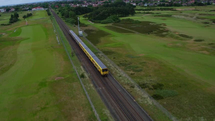 A yellow train travels on tracks near a golf course