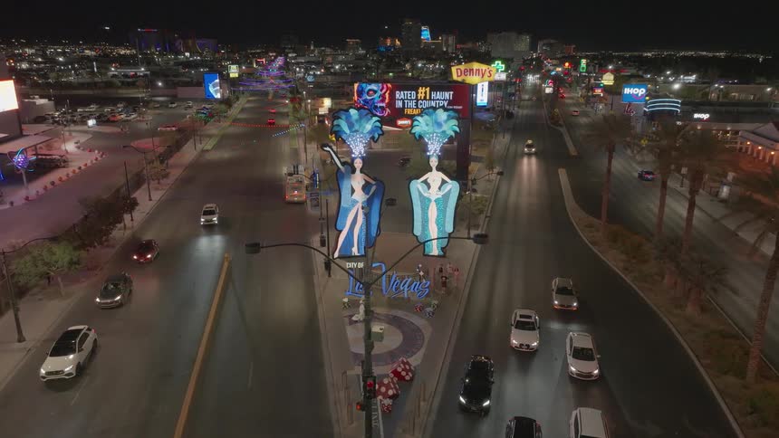 A freeway in Las Vegas at night features numerous billboard ads as a series of cars drive by