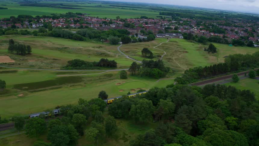 A train travels down a track next to green fields