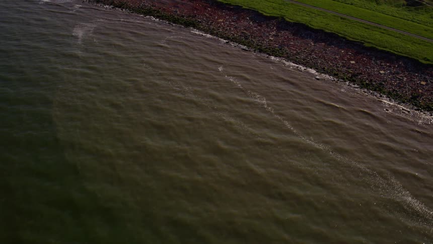 The water is reflecting the sun by the shore