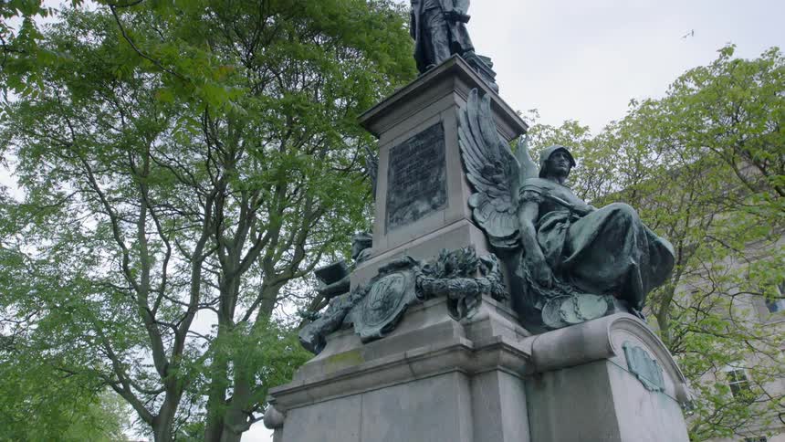 A statue of a man on a monument stands amidst trees under an overcast sky