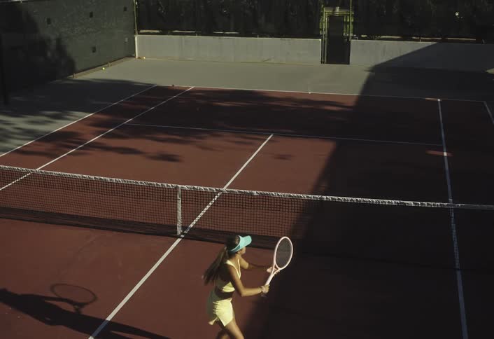The woman is hitting tennis balls from the tennis ball machine