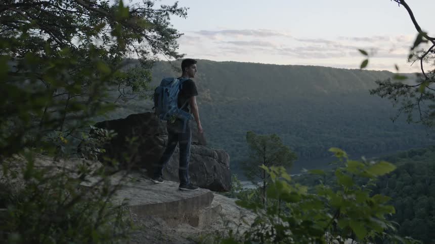 Man walking to the edge of a cliff overlooking hills and water