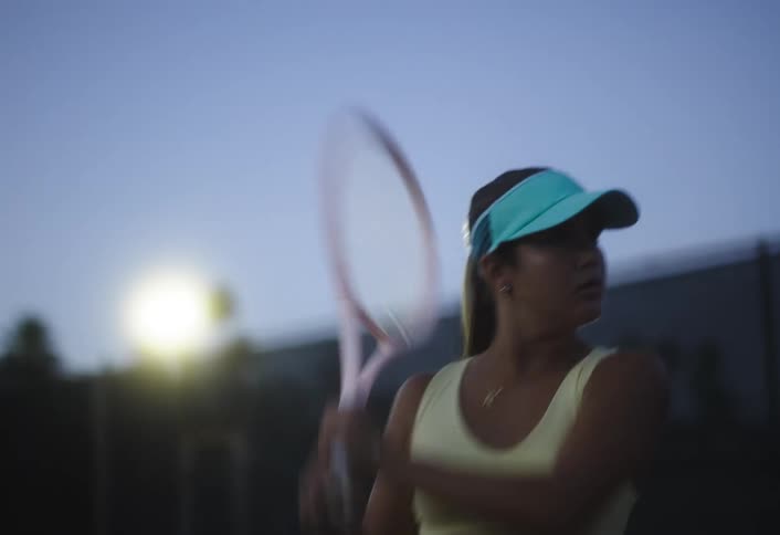 A woman wearing a blue cap is playing tennis with a pink racket and hitting the ball