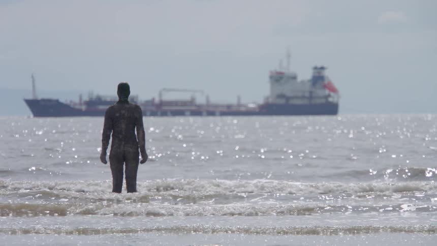 A person with some suit on standing in the water with a large ship in the back