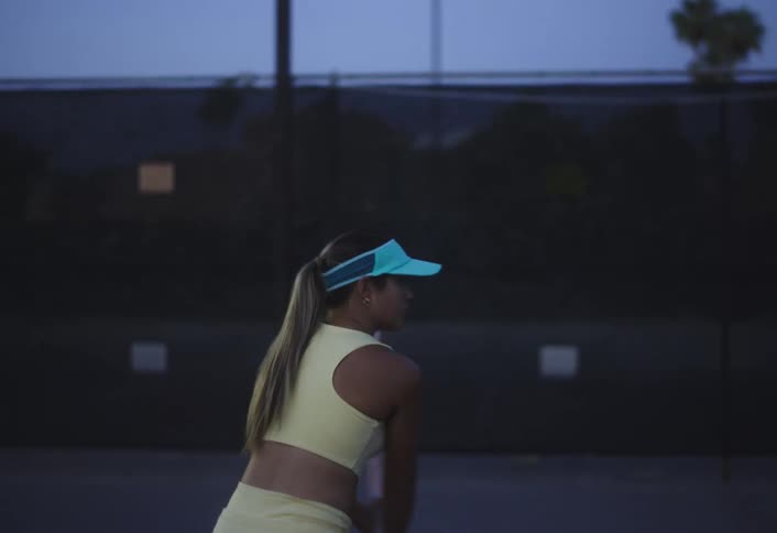 Lady hits tennis ball with the racket at sunset on the tennis court