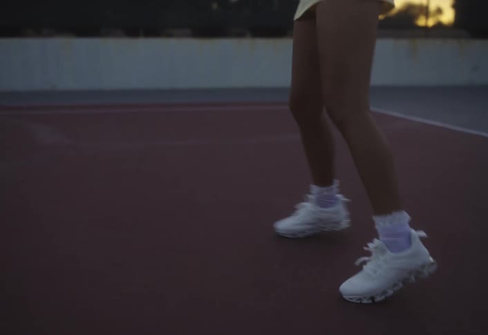 Close up of a female tennis players legs as she moves around while playing tennis in an outdoor court at sunset