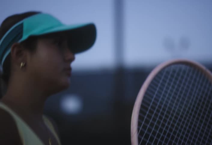 A young woman plays tennis outdoors at dusk focused with racket in hand