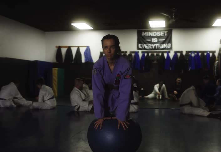 A young girl wearing a purple kung fu uniform balances on a ball during a kung fu training class