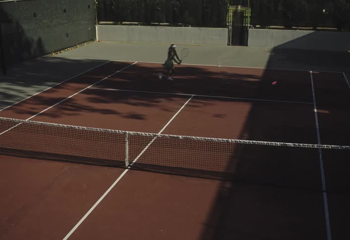 A person plays tennis alone on an empty outdoor court