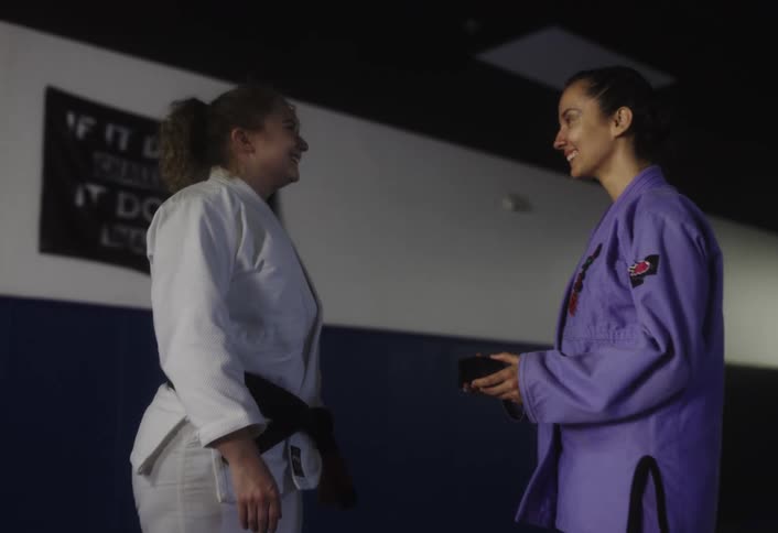 Woman handing another woman a black belt in martial arts
