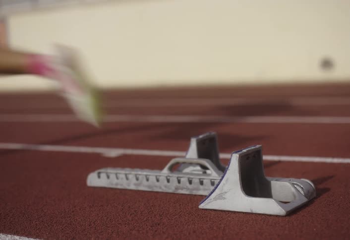 A female athlete sprints off from the starting point of the track around midday