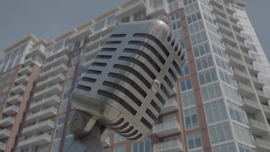 A statue of a microphone stand in front of a multistory building