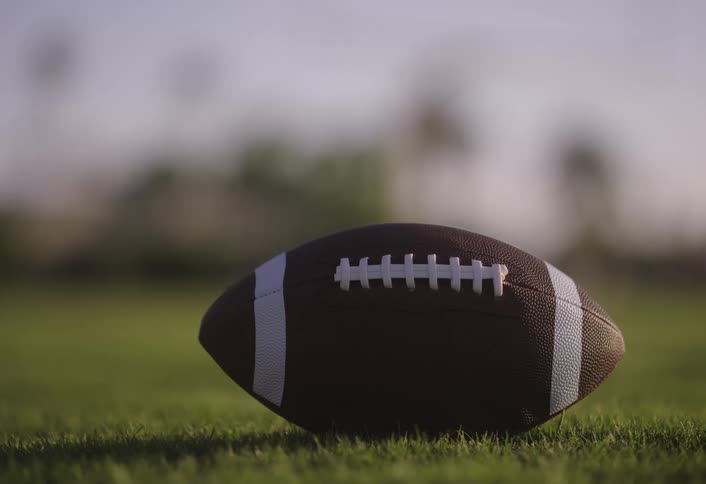 American football laying on green grass on a field