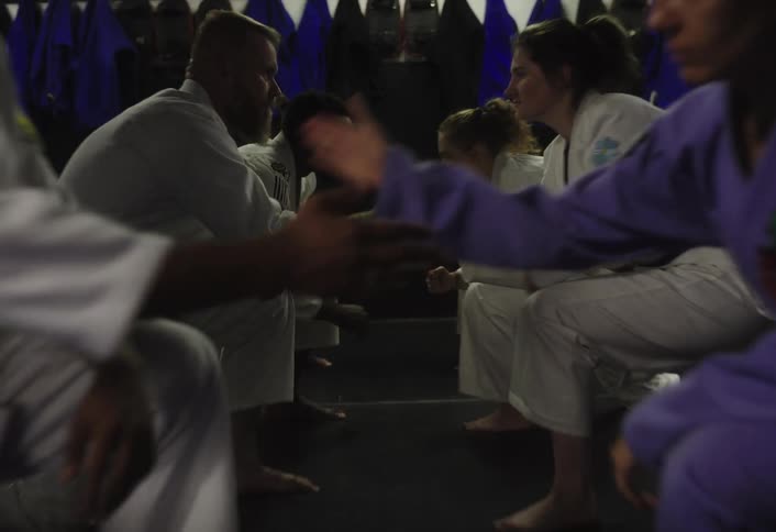 Group ofmartial artists kneel facing each other in a dimly lit dojo
