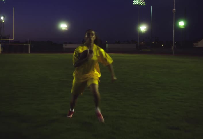 Woman running across a grass field at night with a football