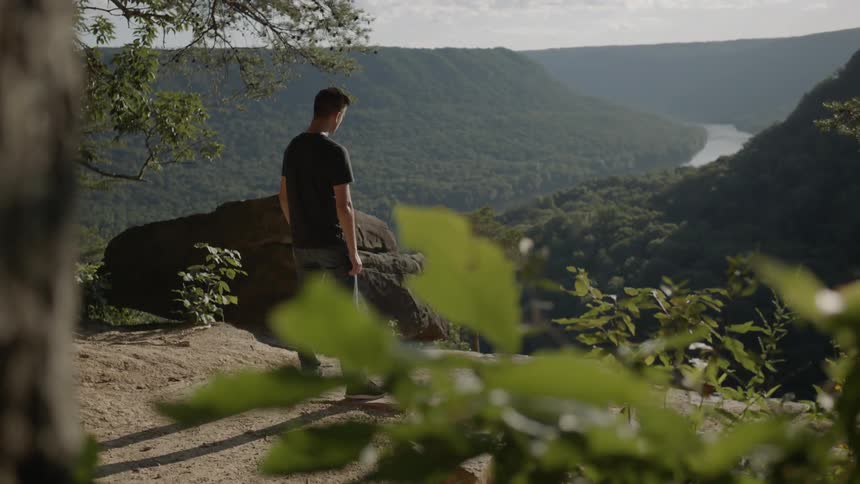 A man stands on a cliff near a valley