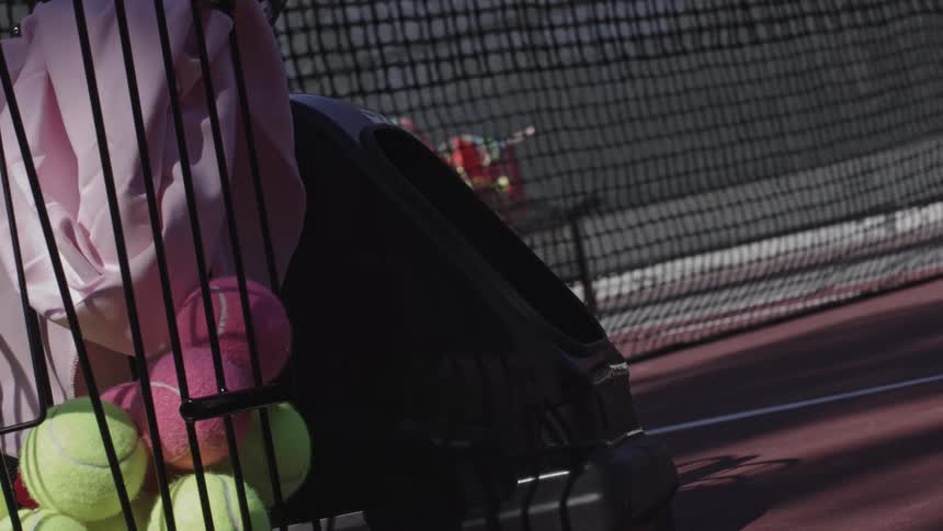 Tennis balls sit in a container on a tennis court