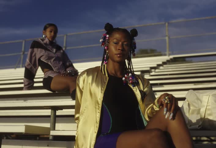 Two young women strike modeling poses on sunny stadium bleachers
