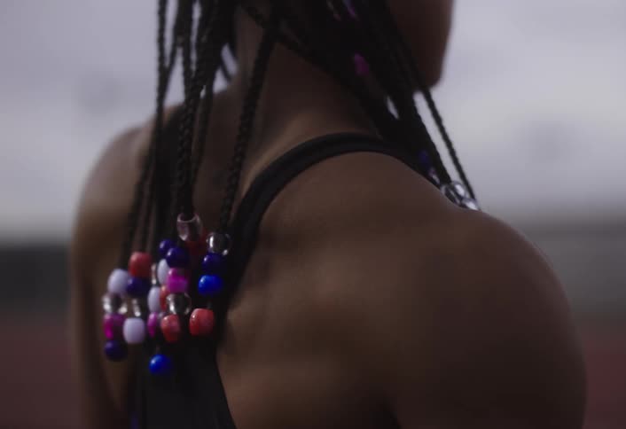 Woman in tank top stretching her shoulders highlighting her dreadlocked hair with colorful stones
