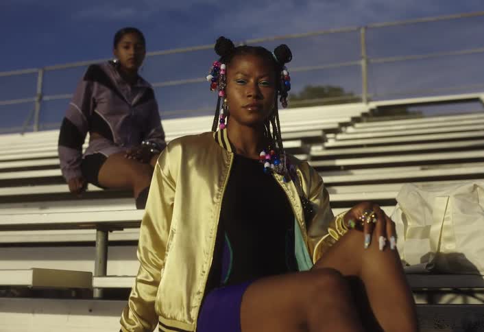 Two black females seated in the stadium stand on different rows at daytime