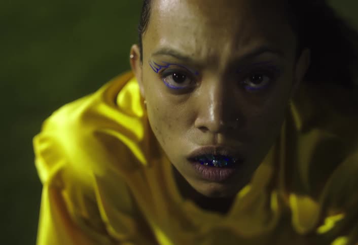 A female football player wearing a yellow jersey and mouthguard catches her breath during a nighttime match