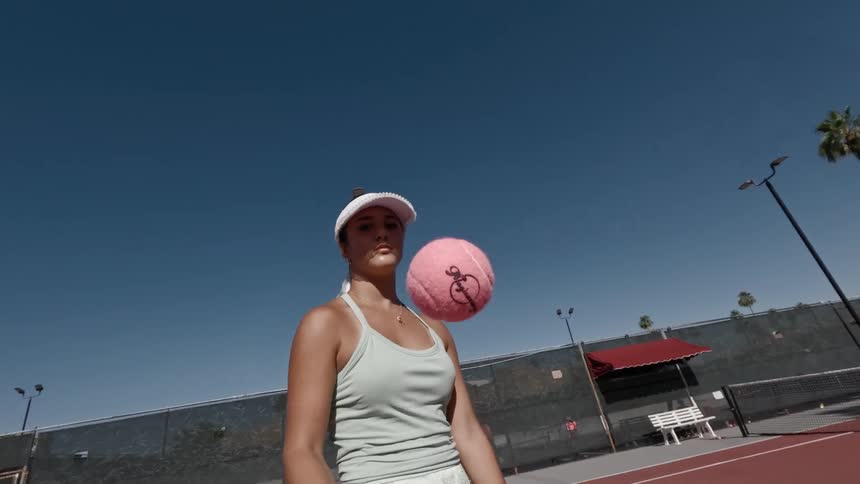 The woman is bouncing a pink tennis ball