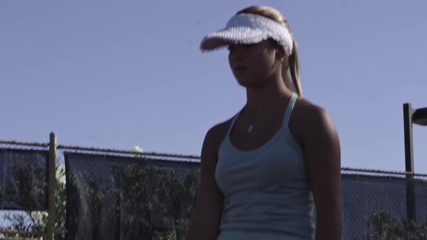 A woman on a tennis court at midday tosses her tennis racket into a 360degree spin and catches it by the handle in a smooth loop