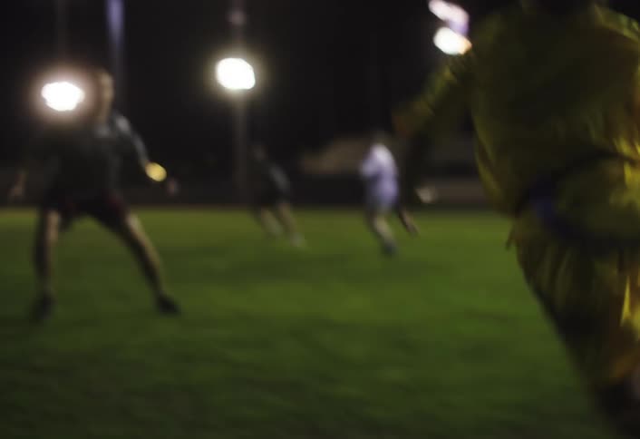 A woman charges on the field with the football at night