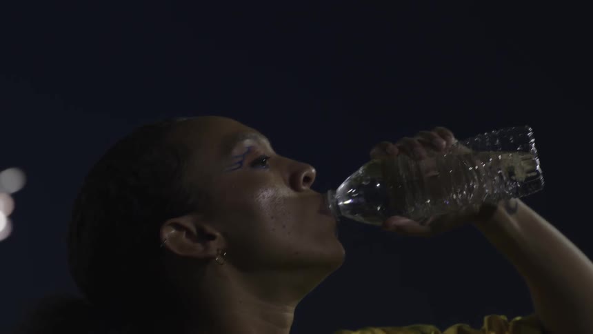 The face of a woman outdoors at night who is drinking water from a bottle