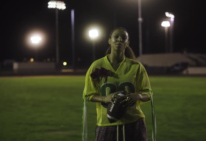 Female athlete holds a football between both hands on a field at night