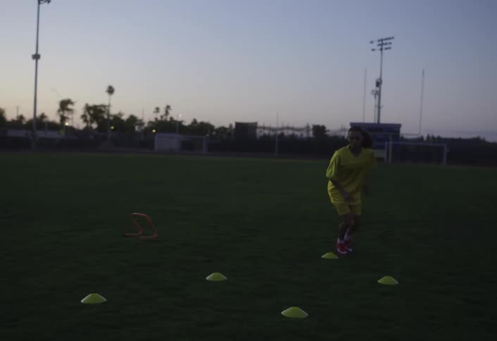 The woman is running around cones on the field