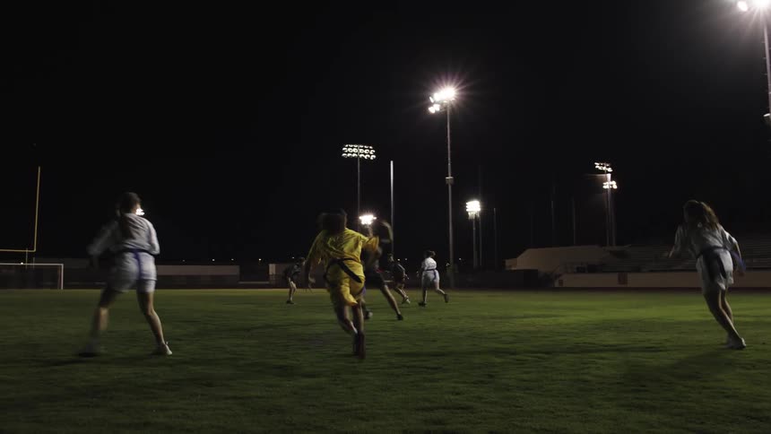 Young athletes play a game of flag football under stadium lights at night