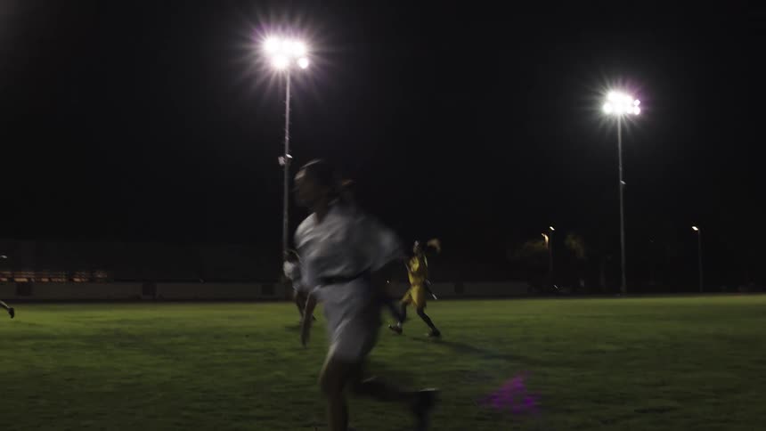Flag football players chase the ball under bright stadium lights at night