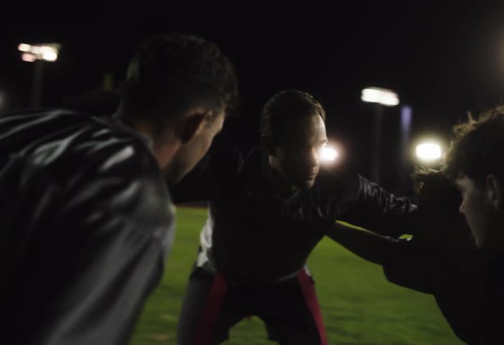 Man talking to young teenagers on a sports field at night