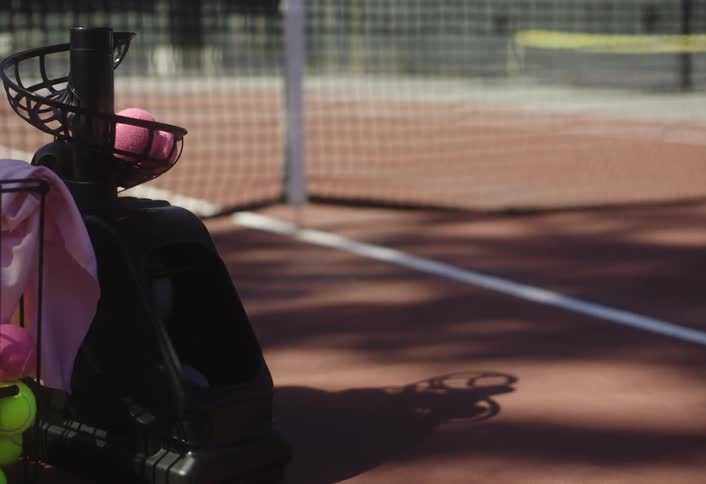 Small tennis ball machine serving pink tennis balls on a court