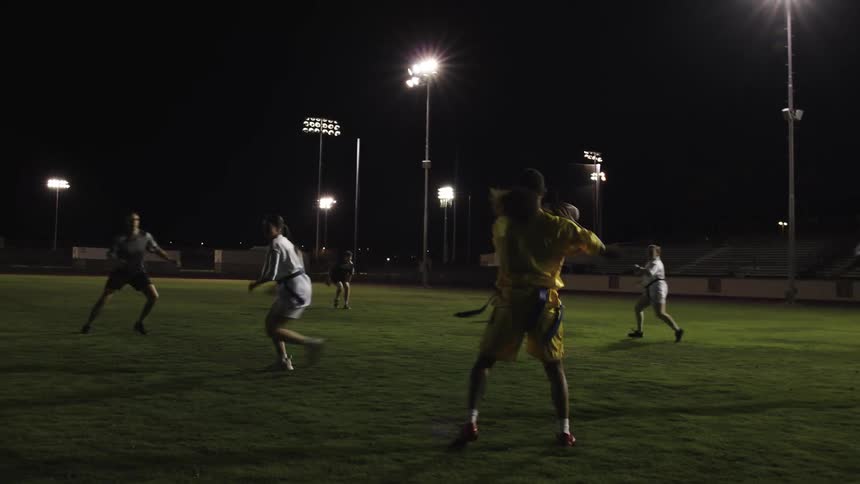 People on a grass field at night playing american football
