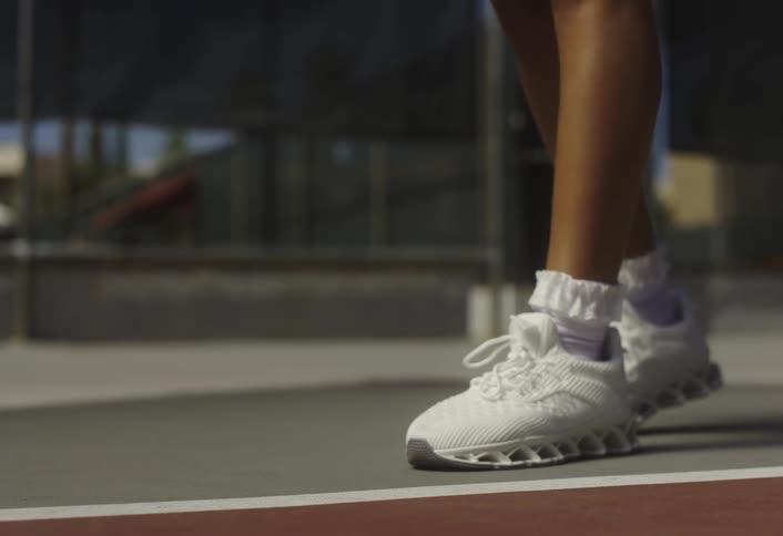 Close up of a female tennis players legs as she continuously bounces a tennis ball while standing in an outdoor court in daytime