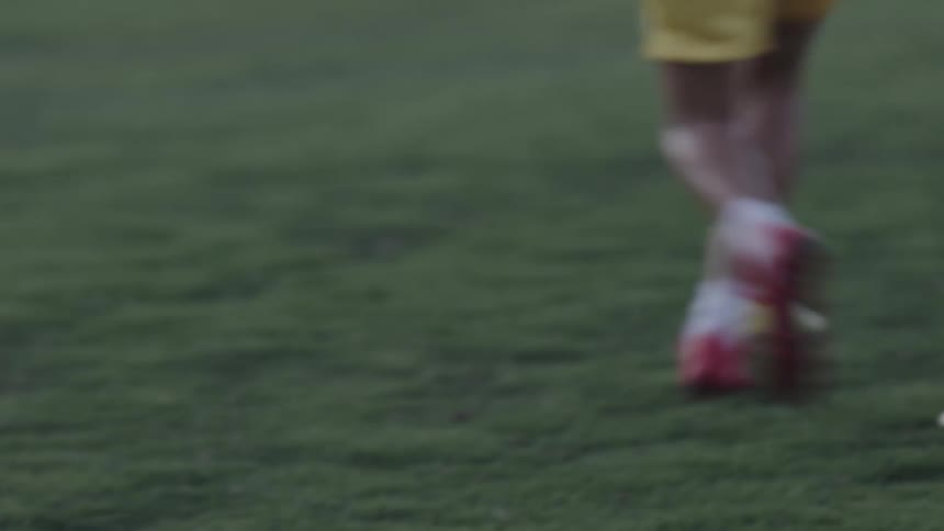 The legs of a person running on a training field on a sports lawn and wearing red cleats